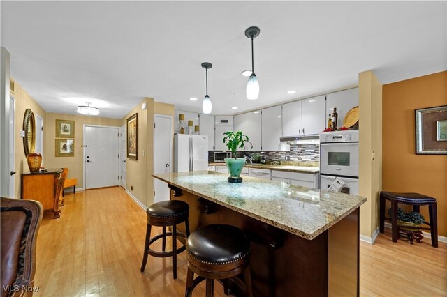 18975 Van Aken Blvd Unit 401, Shaker Heights, OH 44122 - kitchen with white appliances, light wood-type flooring, decorative backsplash, under cabinet range hood, and pendant lighting