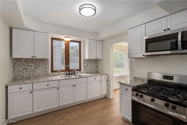 3338 E 130th St, Cleveland, OH 44120 - kitchen featuring stainless steel appliances, a sink, arched walkways, light wood finished floors, and tasteful backsplash