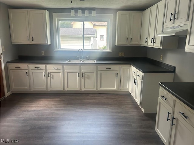 307 N 8th St, Coshocton, OH 43812 - kitchen with a sink, under cabinet range hood, dark countertops, dark wood-style floors, and white cabinetry