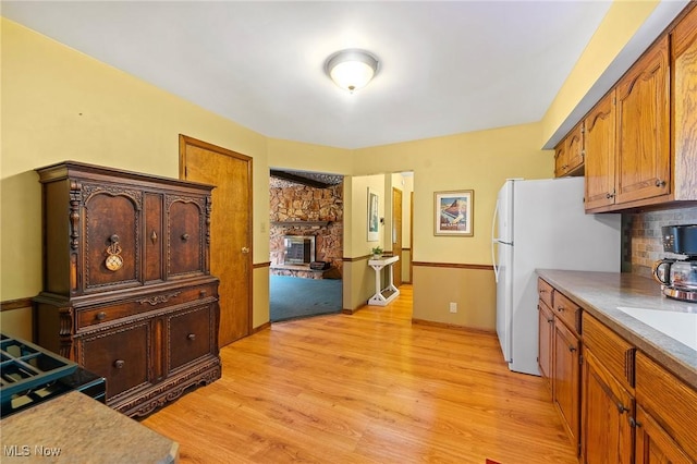 2322 Westview Rd, Cortland, OH 44410 - kitchen with light wood-type flooring, freestanding refrigerator, brown cabinetry, light countertops, and a fireplace