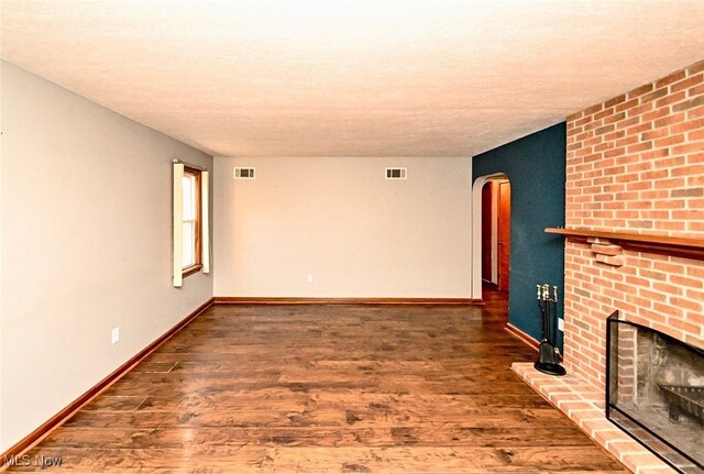 3811 Amherst Ave NW, Massillon, OH 44646 - unfurnished living room featuring arched walkways, wood finished floors, a textured ceiling, and a brick fireplace