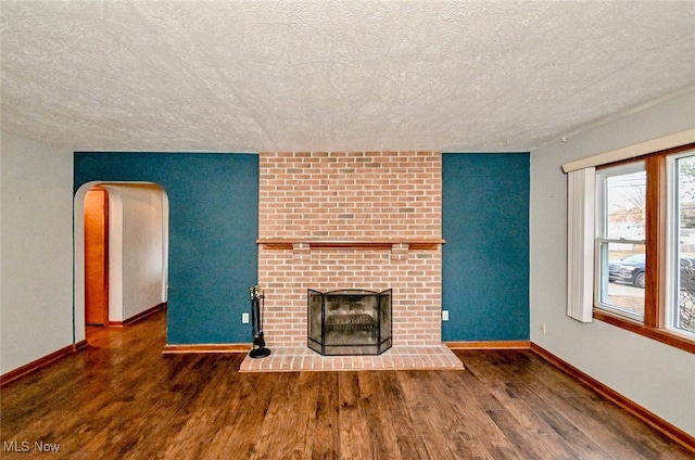 3811 Amherst Ave NW, Massillon, OH 44646 - unfurnished living room with wood finished floors, a brick fireplace, a textured ceiling, and arched walkways