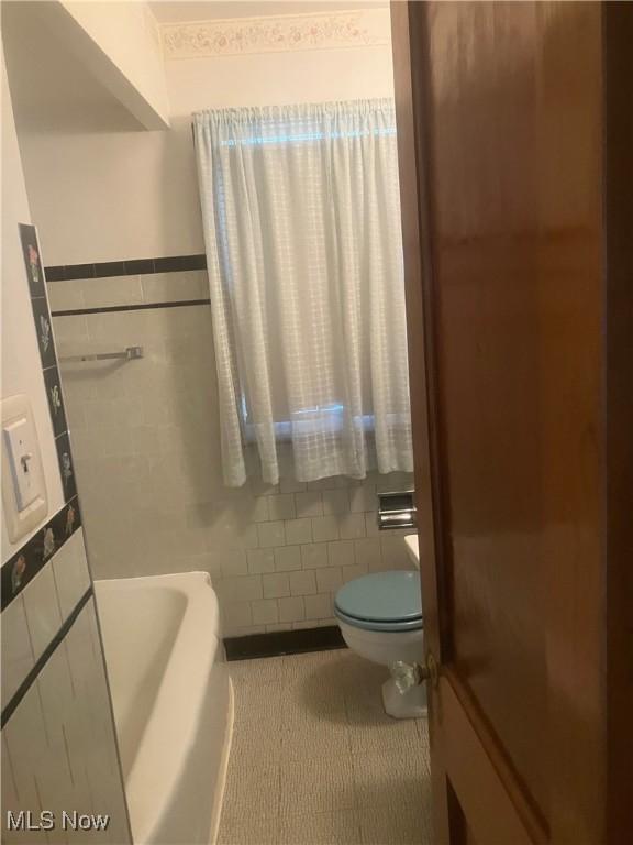 7718 Bertha Ave, Parma, OH 44129 - bathroom featuring tile walls, tile patterned floors, a bath, and wainscoting