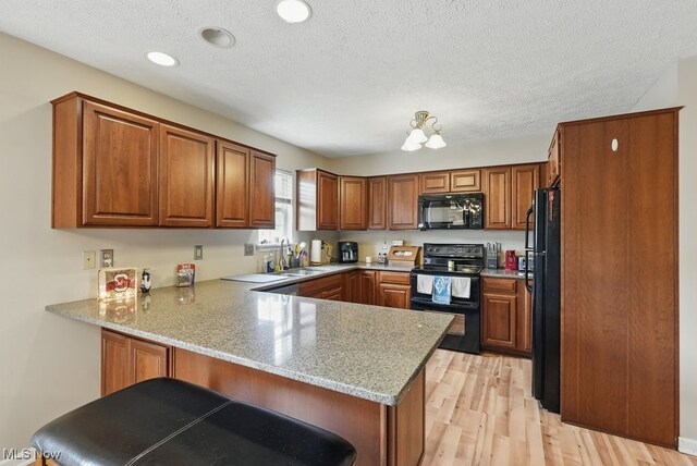 91 Falling Water Cir, Munroe Falls, OH 44262 - kitchen with black appliances, a peninsula, brown cabinets, light wood-style flooring, and a textured ceiling