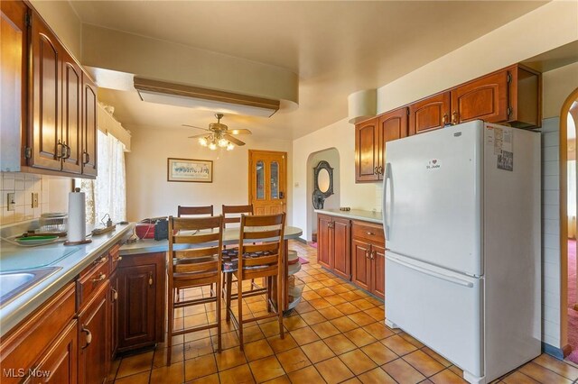 6567 Mount Everett Rd, Hubbard, OH 44425 - kitchen with freestanding refrigerator, ceiling fan, decorative backsplash, arched walkways, and tile patterned flooring