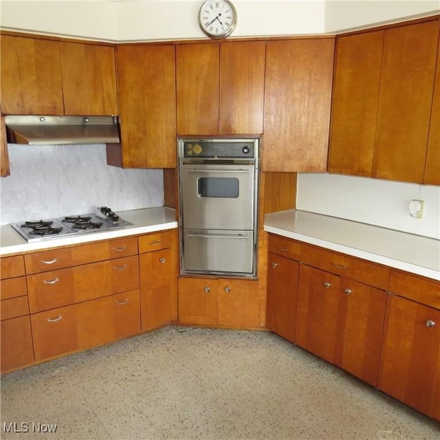 399 N Main St, Amsterdam, OH 43903 - kitchen with under cabinet range hood, stainless steel gas cooktop, brown cabinetry, light countertops, and double wall oven