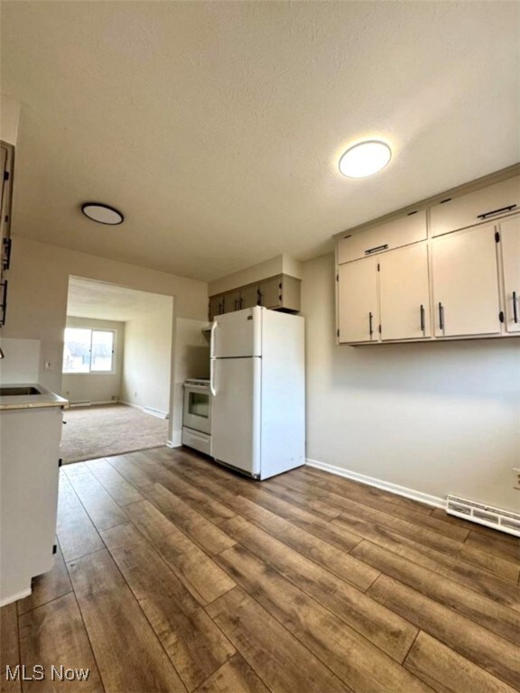 233 Kennedy St, Louisville, OH 44641 - kitchen with freestanding refrigerator, range, dark wood finished floors, white cabinetry, and a baseboard radiator