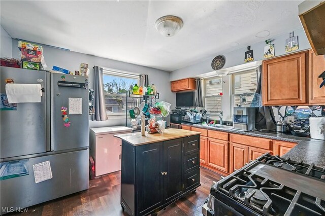 3676 E 69th St, Cleveland, OH 44105 - kitchen with freestanding refrigerator, dark wood-style flooring, gas stove, a kitchen island, and brown cabinetry