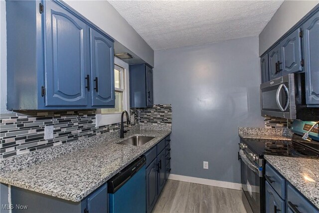 12604 Saint John Ave, Cleveland, OH 44111 - kitchen with stainless steel appliances, blue cabinets, a textured ceiling, light wood-type flooring, and decorative backsplash