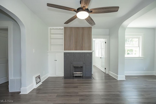 381 Watson St, Akron, OH 44305 - unfurnished living room featuring arched walkways, dark wood finished floors, ceiling fan, built in features, and a fireplace with flush hearth