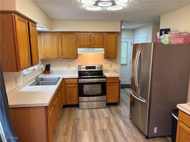 732 E High St, Alliance, OH 44601 - kitchen featuring stainless steel appliances, under cabinet range hood, brown cabinets, light wood-style floors, and a textured ceiling