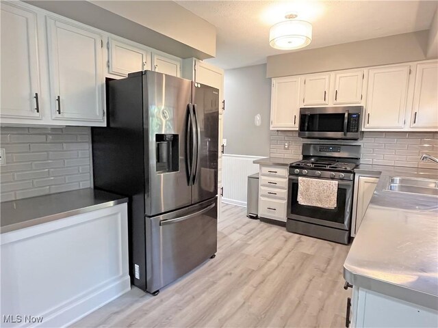 3061 Greenwich Ln, Brunswick, OH 44212 - kitchen featuring stainless steel appliances, white cabinetry, backsplash, wainscoting, and light wood-style flooring