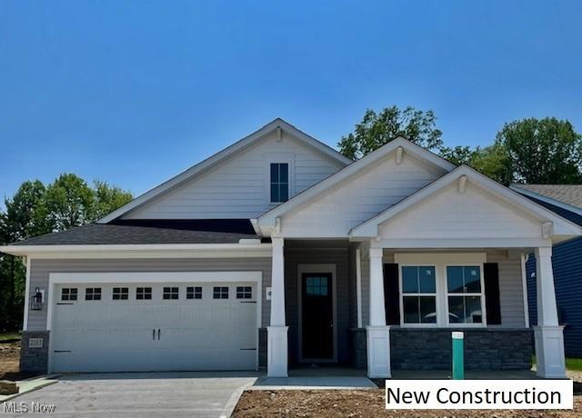 2167 Myla Way, Amherst, OH 44001 - craftsman house featuring a garage, concrete driveway, stone siding, and a porch