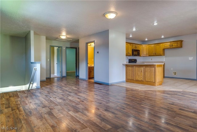 1104 4th St, Belpre, OH 45714 - kitchen with black microwave, light wood-style flooring, open floor plan, brown cabinets, and a textured ceiling