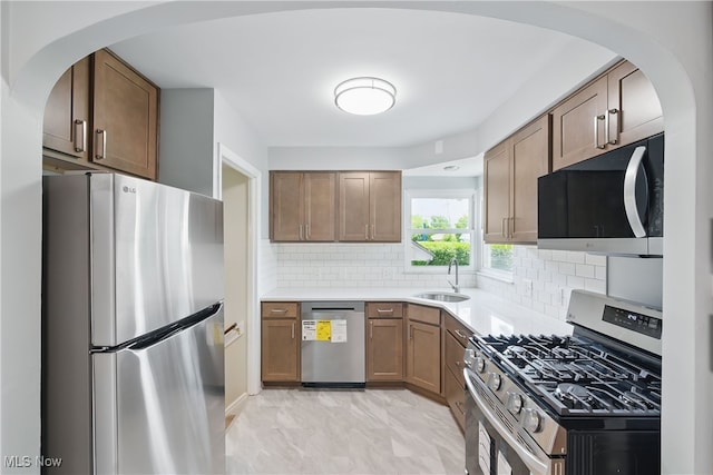 10212 Grace Ave, Garfield Heights, OH 44125 - kitchen featuring stainless steel appliances, backsplash, light countertops, arched walkways, and brown cabinets