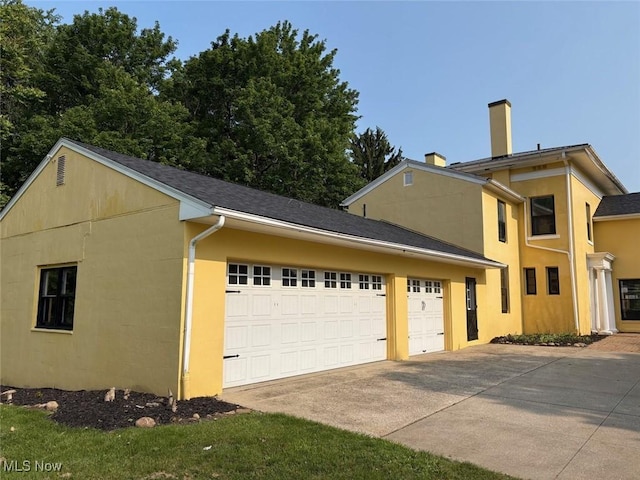 989 Orchard Hill Cir, Massillon, OH 44646 - view of side of home featuring driveway, an attached garage, a chimney, and stucco siding