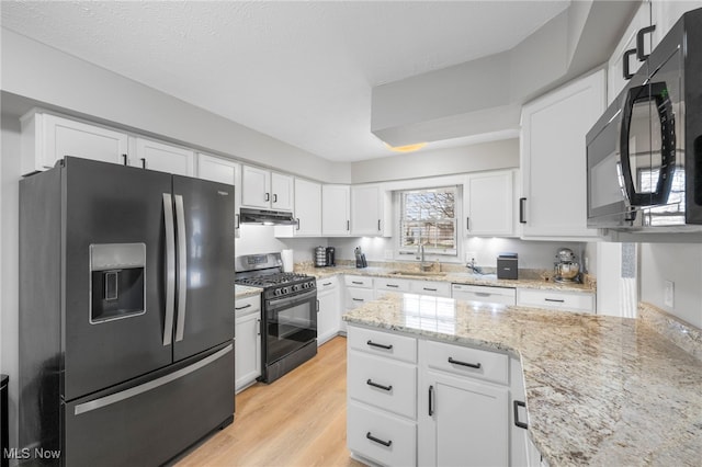 662 2nd St Unit 2, Fairport Harbor, OH 44077 - kitchen with black appliances, under cabinet range hood, white cabinetry, light wood-style floors, and light stone counters