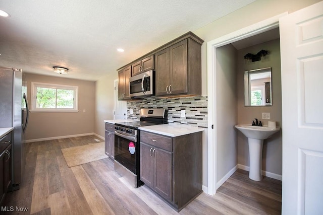 4029 Minard Rd NW, Dover, OH 44622 - kitchen featuring appliances with stainless steel finishes, light wood-type flooring, dark brown cabinets, light countertops, and backsplash