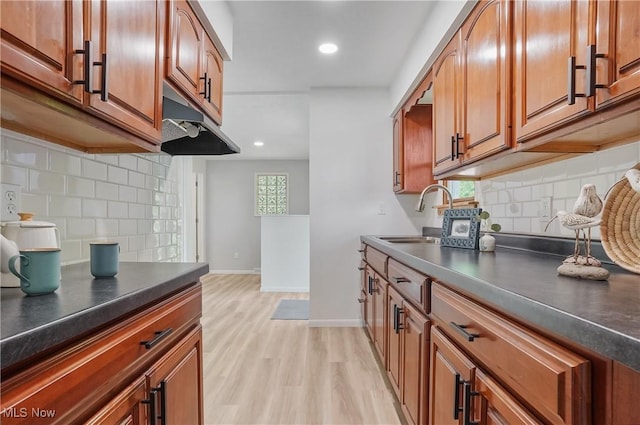 935 Portage Lakes Dr, Coventry Township, OH 44319 - kitchen featuring dark countertops, tasteful backsplash, brown cabinetry, light wood-style floors, and under cabinet range hood