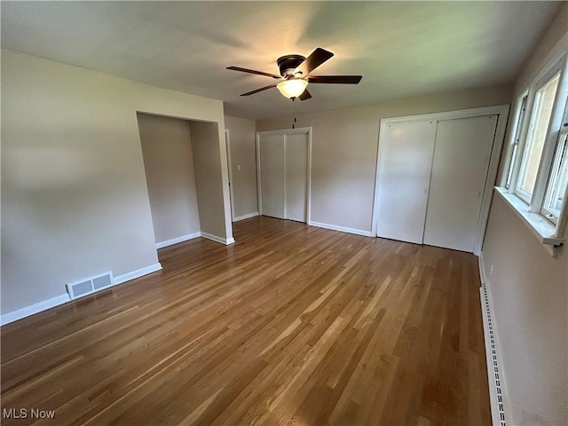 7295 Clovermeade Ave, Poland, OH 44514 - unfurnished bedroom with baseboard heating, wood finished floors, a ceiling fan, and two closets