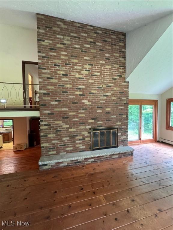 9999 Kirtland Chardon Rd, Chardon, OH 44024 - unfurnished living room featuring wood-type flooring, a baseboard radiator, a fireplace, a high ceiling, and a textured ceiling