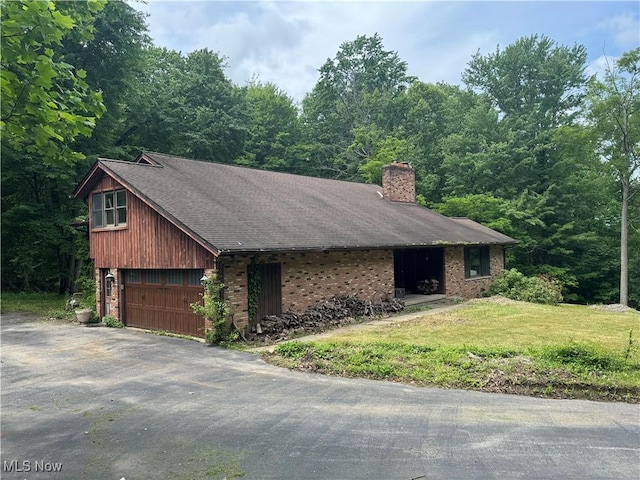 9999 Kirtland Chardon Rd, Chardon, OH 44024 - view of side of property featuring a garage, a chimney, driveway, brick siding, and a lawn