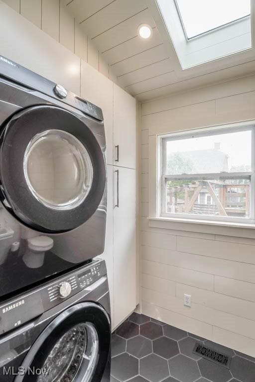 1004 Clarendon Ave SW, Canton, OH 44710 - washroom with stacked washer and clothes dryer, a skylight, cabinet space, and dark tile patterned floors