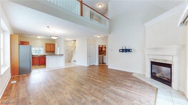 44 Gullybrook Ln, Willoughby, OH 44094 - unfurnished living room with light wood-type flooring, a tiled fireplace, washer / clothes dryer, a high ceiling, and stairway