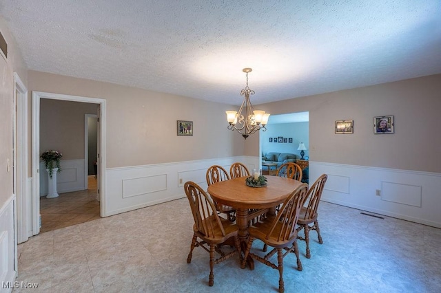 106 Wedgewood Dr, Parkersburg, WV 26104 - dining room with a chandelier, wainscoting, a textured ceiling, and a decorative wall