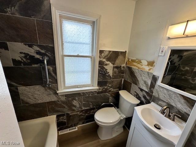 21316 Watson Rd, Maple Heights, OH 44137 - full bathroom with tile walls, vanity, a tub to relax in, wood finished floors, and a wainscoted wall