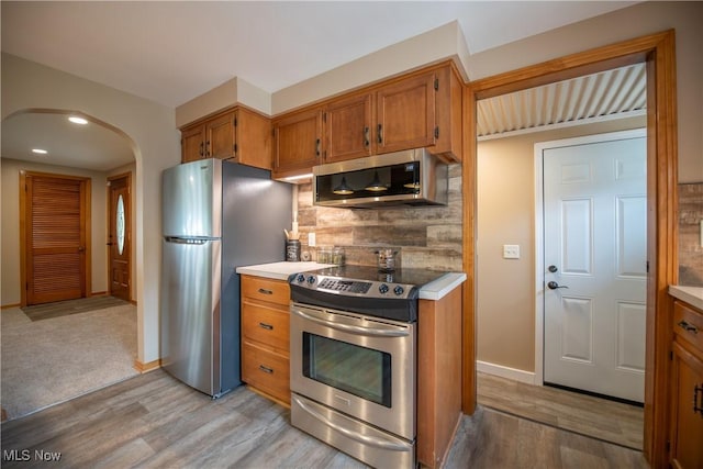 809 Mcdaniel Ave, Minerva, OH 44657 - kitchen with stainless steel appliances, arched walkways, light wood-style flooring, brown cabinets, and decorative backsplash