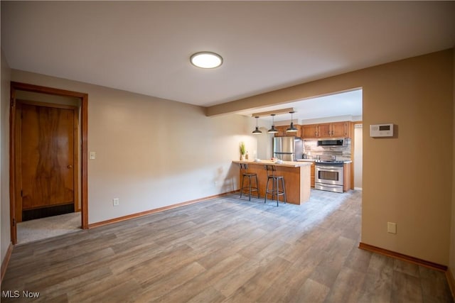 809 Mcdaniel Ave, Minerva, OH 44657 - kitchen with appliances with stainless steel finishes, a peninsula, a kitchen breakfast bar, light wood finished floors, and brown cabinets