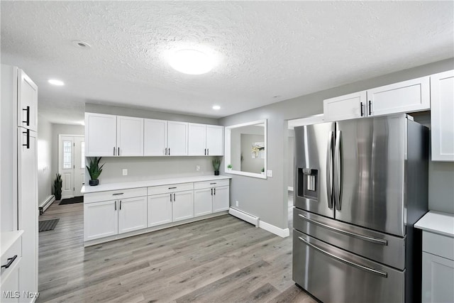 5417 Edgewood Dr, Lorain, OH 44053 - kitchen with stainless steel refrigerator with ice dispenser, light countertops, a baseboard heating unit, a textured ceiling, and light wood-style floors