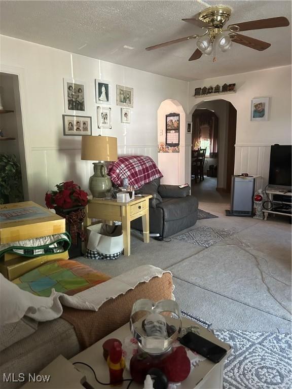 3601 State St, Weirton, WV 26062 - carpeted living room featuring arched walkways, a ceiling fan, a decorative wall, wainscoting, and a textured ceiling