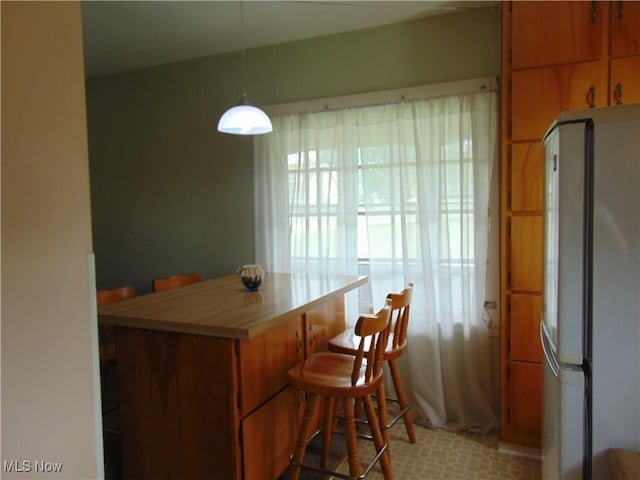 4017 N Ridge Rd W, Saybrook, OH 44004 - kitchen featuring freestanding refrigerator, a breakfast bar area, light countertops, brown cabinetry, and decorative light fixtures