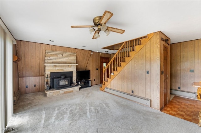 52 Arbor Rd NE, Minerva, OH 44657 - unfurnished living room with a baseboard radiator, wooden walls, a ceiling fan, stairway, and a wood stove