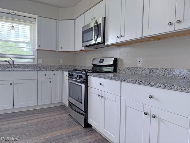 7247 Kiltie Ln, Northfield, OH 44067 - kitchen featuring stainless steel appliances, white cabinets, light stone counters, wood finished floors, and decorative light fixtures