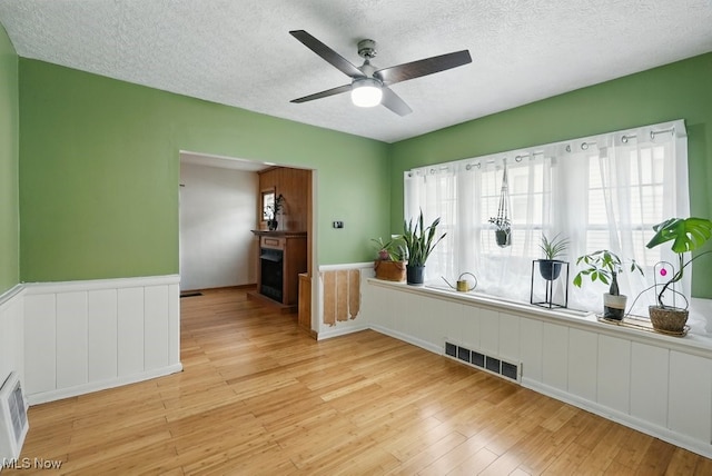447 Allenford St, Akron, OH 44314 - empty room with light wood finished floors, wainscoting, ceiling fan, a textured ceiling, and a fireplace