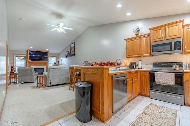 10393 Scotney Ave NW, North Canton, OH 44720 - kitchen featuring appliances with stainless steel finishes, a ceiling fan, a fireplace, a peninsula, and lofted ceiling