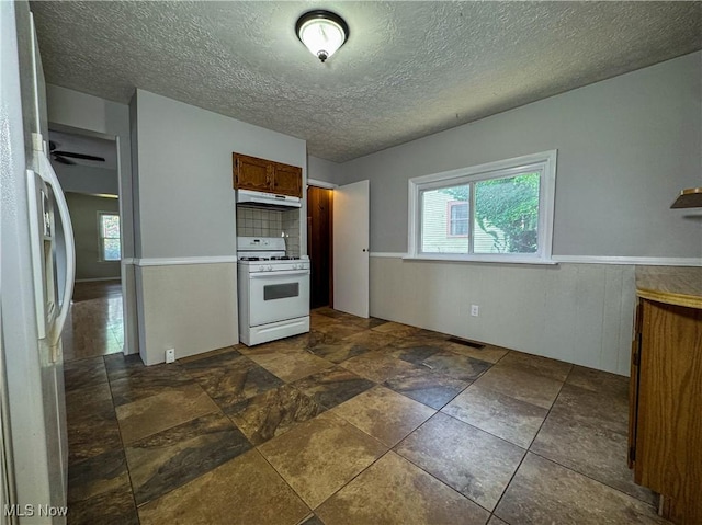 101 Ridgeway St, Struthers, OH 44471 - kitchen featuring white appliances, under cabinet range hood, plenty of natural light, brown cabinets, and a wainscoted wall