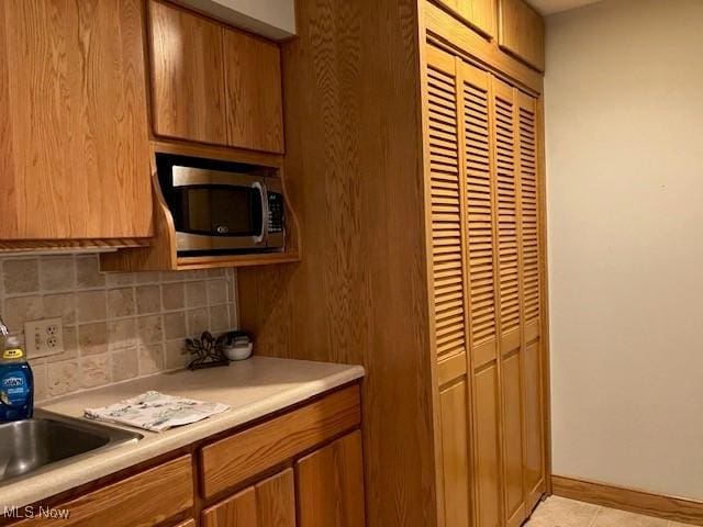 625 Canterbury Ln Unit 27A, Medina, OH 44256 - kitchen with stainless steel microwave, backsplash, light countertops, brown cabinets, and light tile patterned flooring