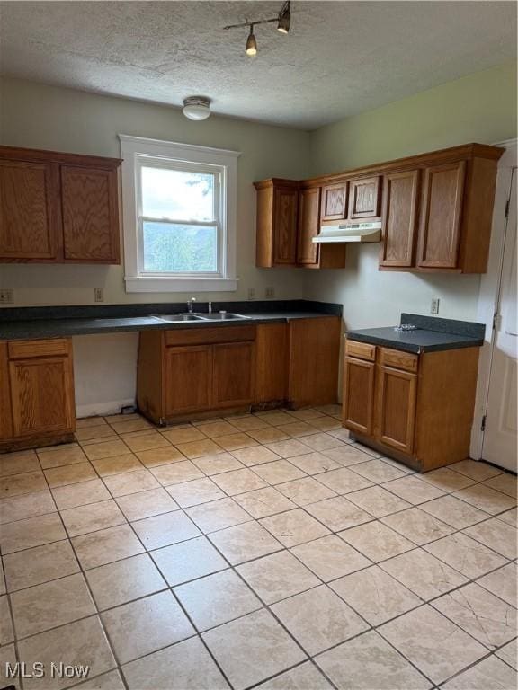 1225 Shorb Ave NW, Canton, OH 44703 - kitchen with under cabinet range hood, brown cabinets, a textured ceiling, light tile patterned floors, and dark countertops