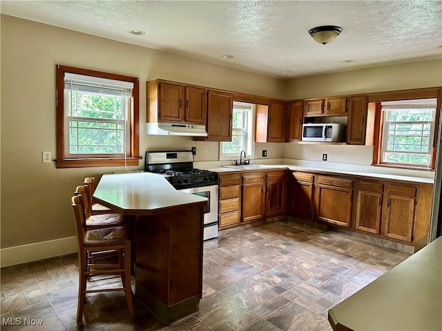 25 W Water St, Hubbard, OH 44425 - kitchen featuring stainless steel appliances, under cabinet range hood, brown cabinets, a textured ceiling, and healthy amount of natural light