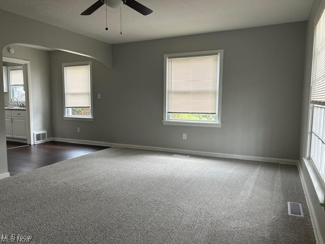 1975 9th St SW, Akron, OH 44314 - empty room with dark colored carpet, arched walkways, ceiling fan, and plenty of natural light