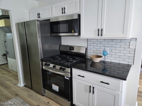 7611 Liberty Ave, Parma, OH 44129 - kitchen with stainless steel appliances, light wood-type flooring, white cabinetry, decorative backsplash, and dark stone counters