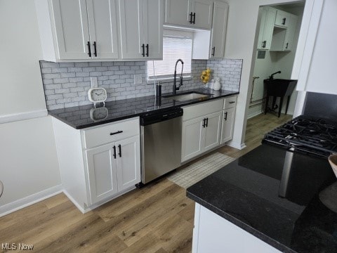 7611 Liberty Ave, Parma, OH 44129 - kitchen featuring stainless steel dishwasher, decorative backsplash, light wood-style floors, white cabinets, and dark stone counters