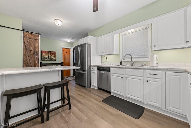 4000 Kenneth Rd, Stow, OH 44224 - kitchen featuring appliances with stainless steel finishes, light wood-type flooring, white cabinetry, a barn door, and a breakfast bar