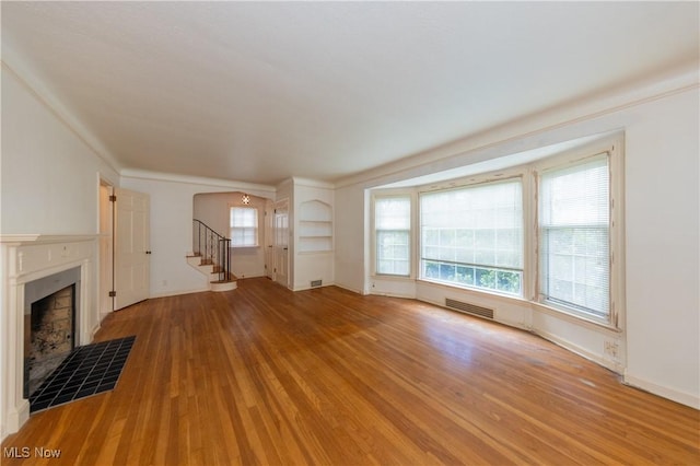 3526 Raymont Blvd, University Heights, OH 44118 - unfurnished living room with light wood-type flooring, a tile fireplace, stairs, arched walkways, and crown molding