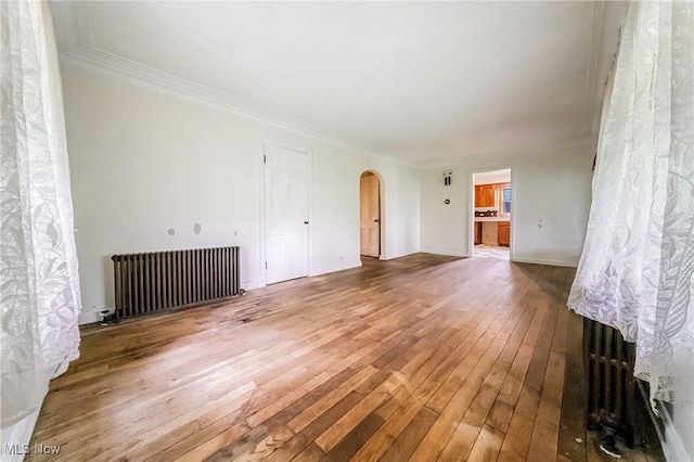 9509 Reed Rd, Columbia Station, OH 44028 - unfurnished living room with radiator heating unit, arched walkways, hardwood / wood-style flooring, and crown molding