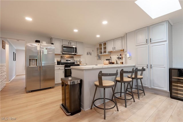7080 Wren Ave NW, North Canton, OH 44720 - kitchen featuring appliances with stainless steel finishes, wine cooler, a kitchen bar, glass insert cabinets, and light wood-style floors